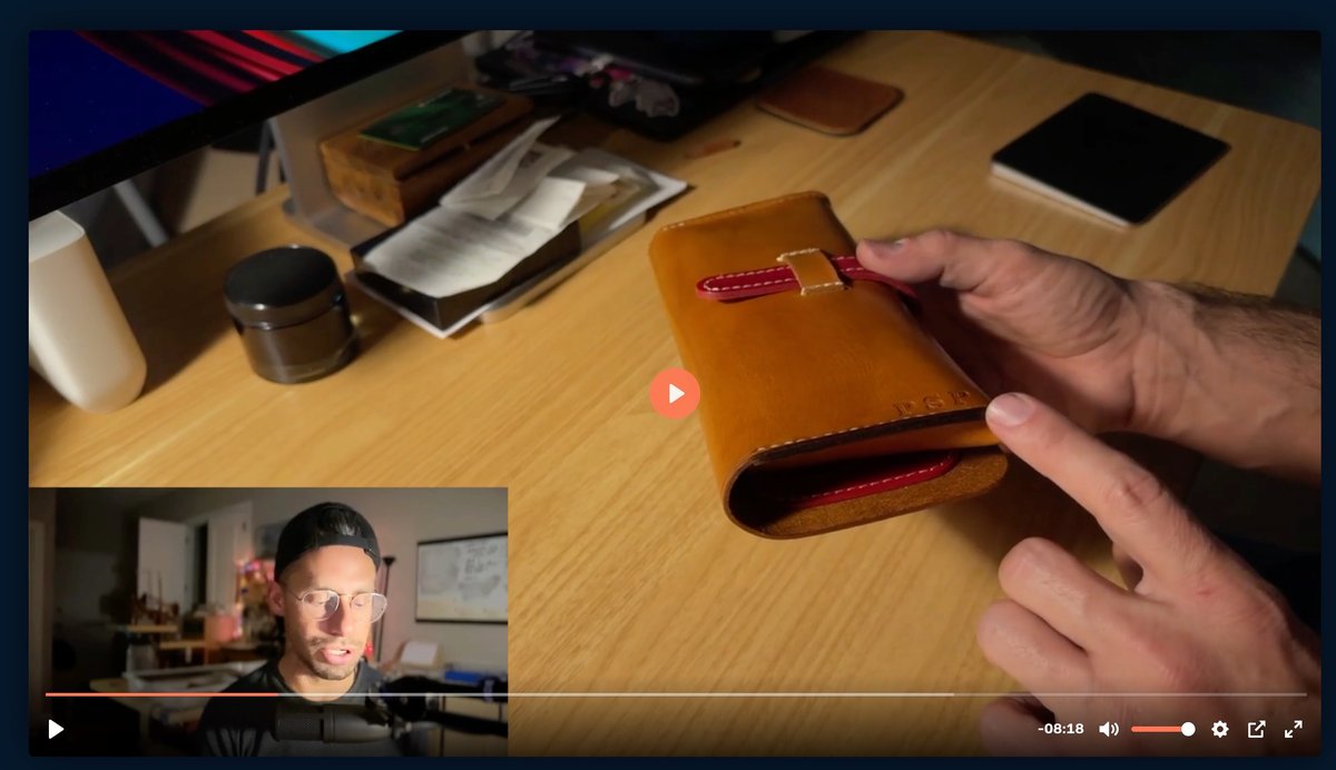 Hand holding an open tan leather wallet with red stitching on a wooden desk during a video presentation.