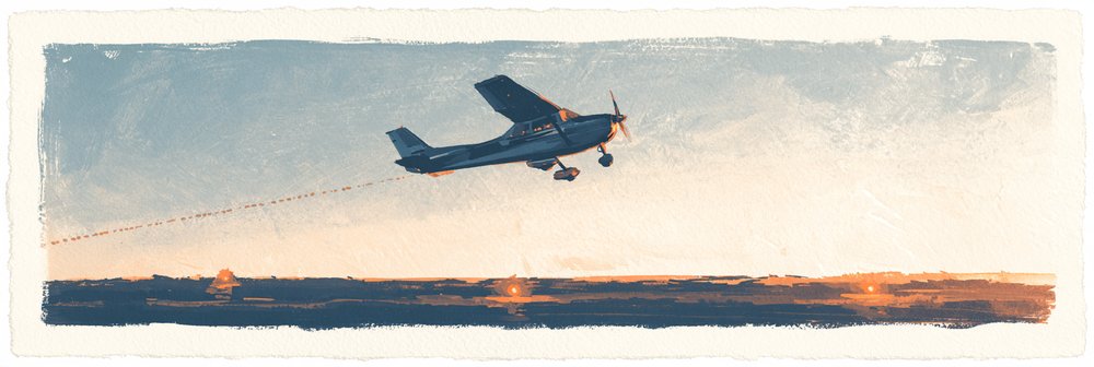 A small blue aircraft flies across a pale sky with a dashed contrail behind it, above a dark landscape lit by a golden sunset.